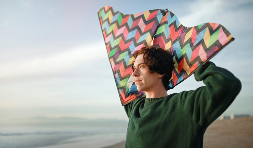Adolescent relaxat, care ține un zmeu colorat deasupra capului