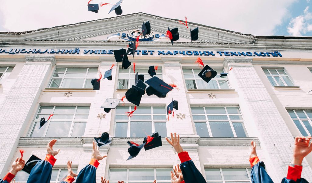 Studenți care aruncă în aer pălăriile de celebrare a finalizării educației