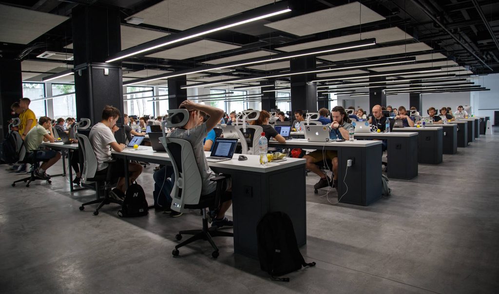 Birou mare, open space, plin de angajați care lucrează la laptopuri