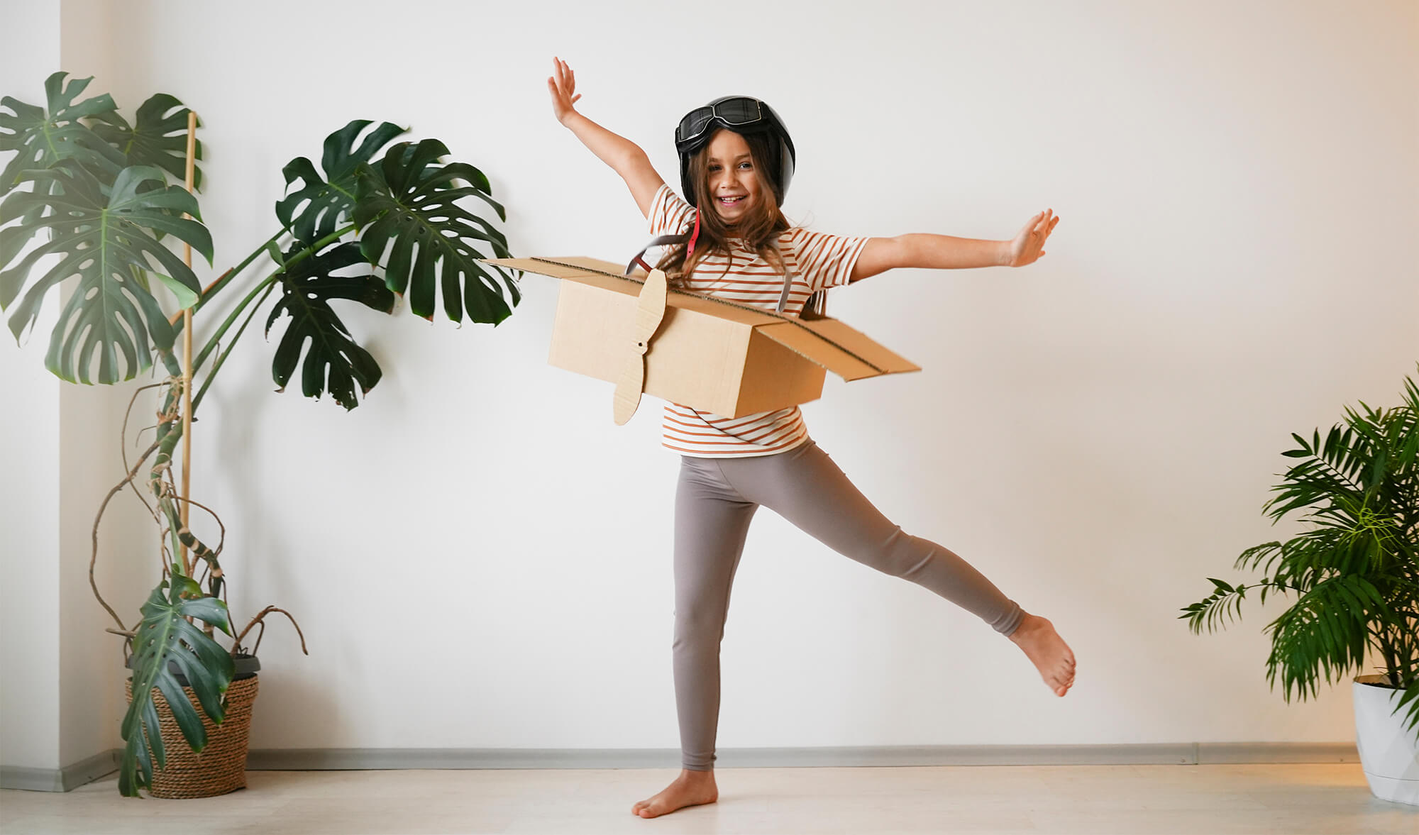 Un copil, începător, plin de imaginație își trăiește bucuria zborului, purtând cu entuziasm un avion din carton.