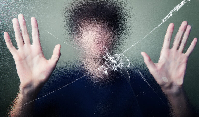 O figură neclarā se sprijină de sticla crăpată, simbolizând suferința, închiderea emoțională și lupta de a se elibera.